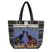 A tote bag with black and white geometric patterned borders, featuring a central tapestry-style panel with two elephants facing each other on a purple background. The handles are black with white text, and a small white brand label is visible near the top zipper.