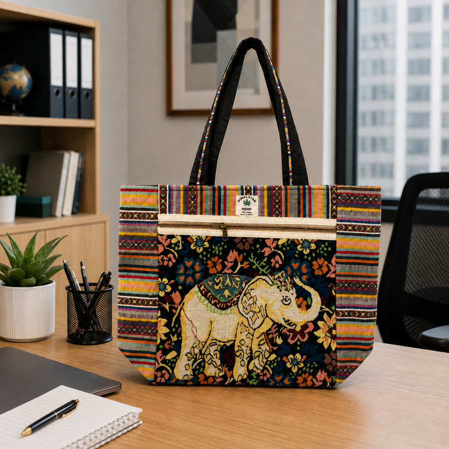 A tote bag with a colorful striped border and a central elephant print on a dark background, displayed on a wooden desk in an office setting.