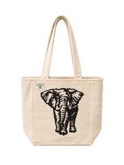 A natural canvas tote bag with a black elephant graphic print on the front and a small green circular brand tag on the upper left, shown against a plain off-white background.