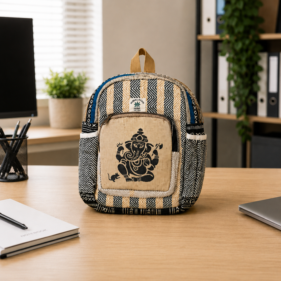 A small backpack with a beige Ganesha graphic on the front, set on a wooden desk in a modern office environment.